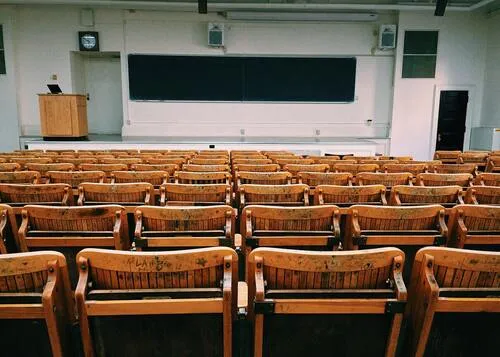 Auditorio vacío con filas de asientos de madera y un tablero al fondo