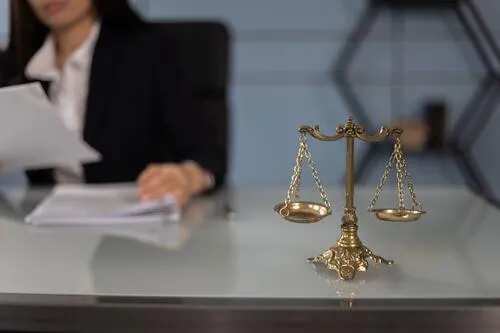 Balanza dorada de la justicia sobre un escritorio, tras la que una mujer de traje revisa papeles