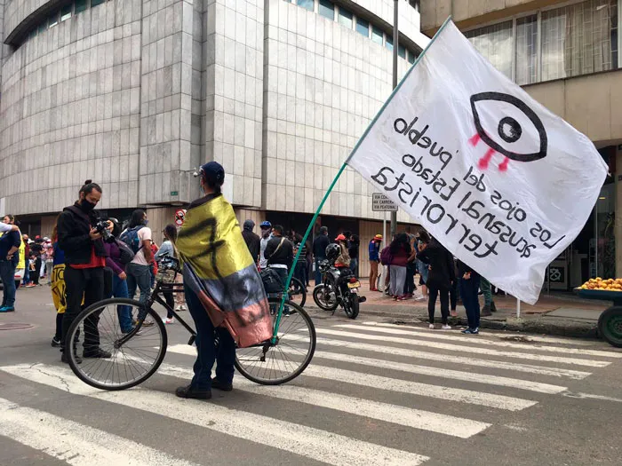 Manifestantes en bicicleta con una bandera blanca con un ojo dibujado en el Paro Nacional en Bogotá