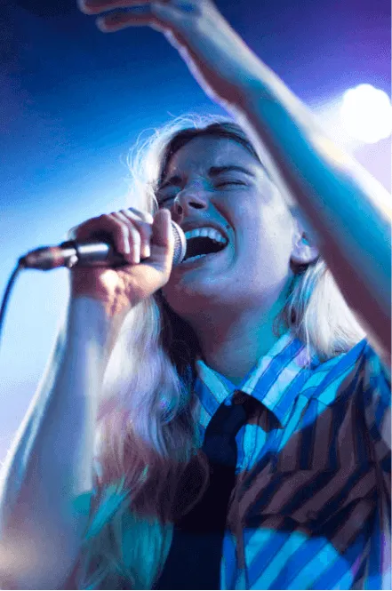 Cantante rubia con micrófono levanta un brazo bajo luces azules en un concierto