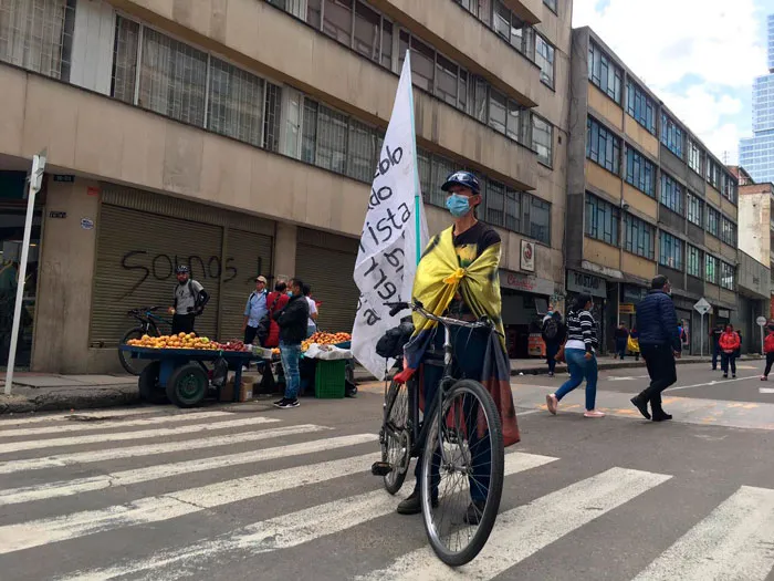 Ciclista con bandera de Colombia sobre los hombros y una bandera blanca en un cruce peatonal de Bogotá