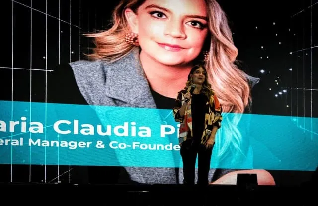 Conferencista de pie en el escenario ante una gran pantalla con su retrato y el cargo «General Manager & Co-Founder»
