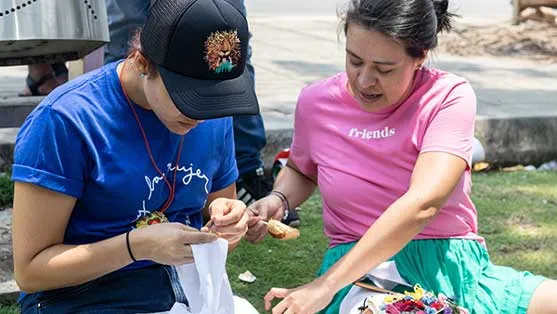 Dos mujeres bordando una tela sentadas en el pasto durante el 8M en Bucaramanga