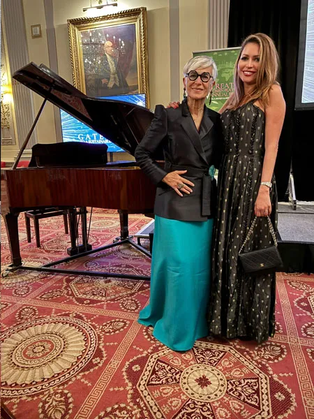 Dos mujeres posan de pie junto a un piano de cola en un salón con alfombra decorada