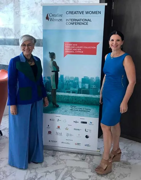 Dos mujeres posan junto a un roll up de la conferencia internacional «Creative Women»