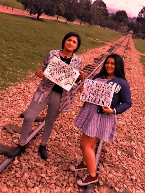 Dos mujeres posan sobre unas vías de tren con carteles escritos a mano