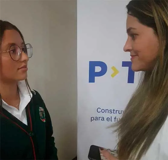 Estudiante con uniforme escolar y una mujer conversan frente a un cartel de P-TECH