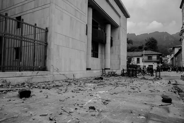 Fachada de un edificio con escombros y piedras en la calle tras una protesta, en blanco y negro