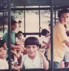 Un niño y otras personas sentados junto a una ventana con reja, en una fotografía antigua