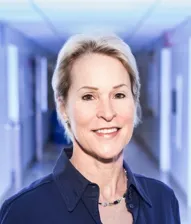 Retrato de Frances H. Arnold, mujer de cabello canoso y camisa azul oscuro, sonriendo en un pasillo