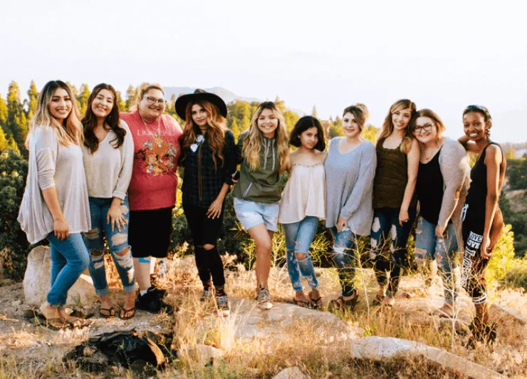 Grupo de once mujeres posando juntas al aire libre entre rocas y pasto seco