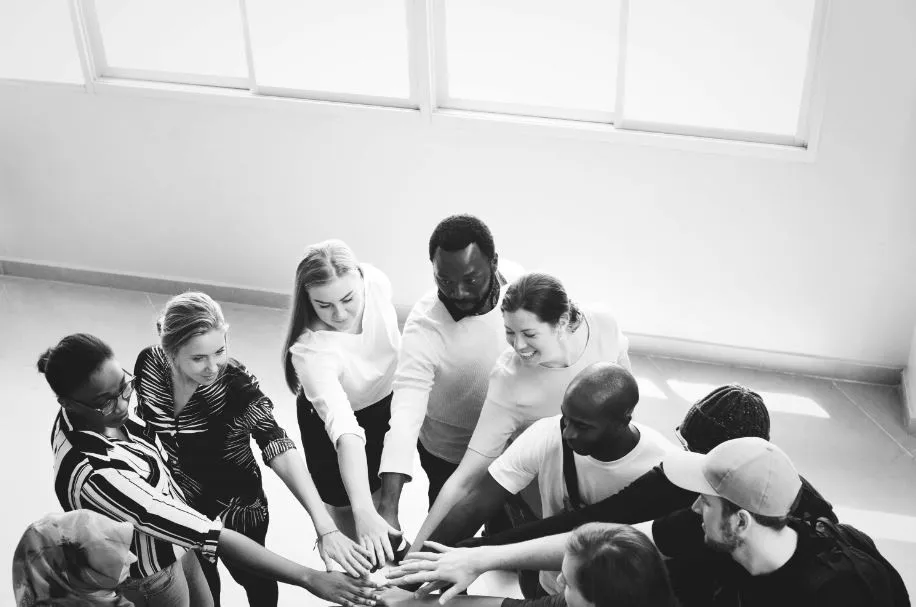 Grupo diverso de personas apilando las manos en círculo, en blanco y negro