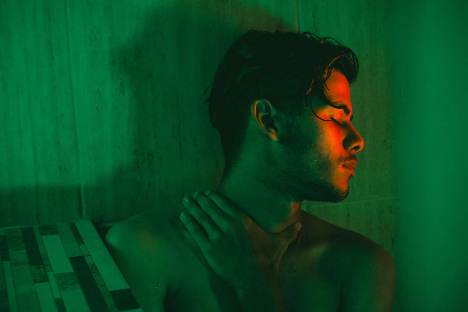 Perfil de un hombre joven con los ojos cerrados iluminado con luz verde y naranja