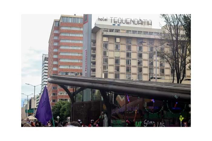 Manifestantes con banderas moradas bajo un puente peatonal frente a edificios de Bogotá el 8 de marzo de 2021