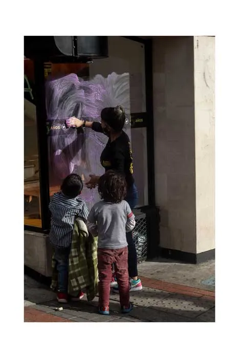 Dos personas pintan sobre el vidrio de un edificio durante la huelga del 8 de marzo de 2021