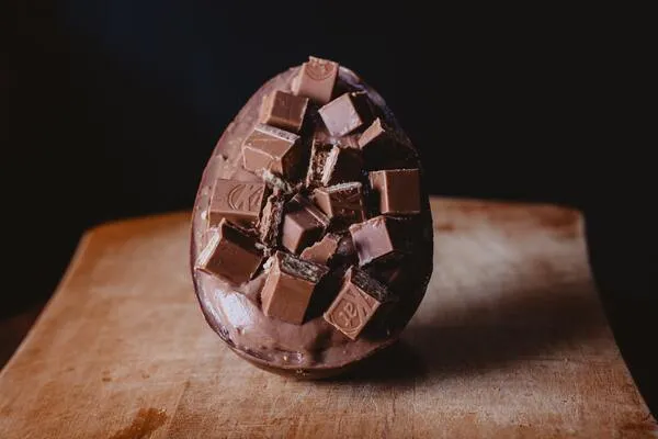 Huevo de chocolate con trozos de chocolate encima sobre una tabla de madera y fondo negro