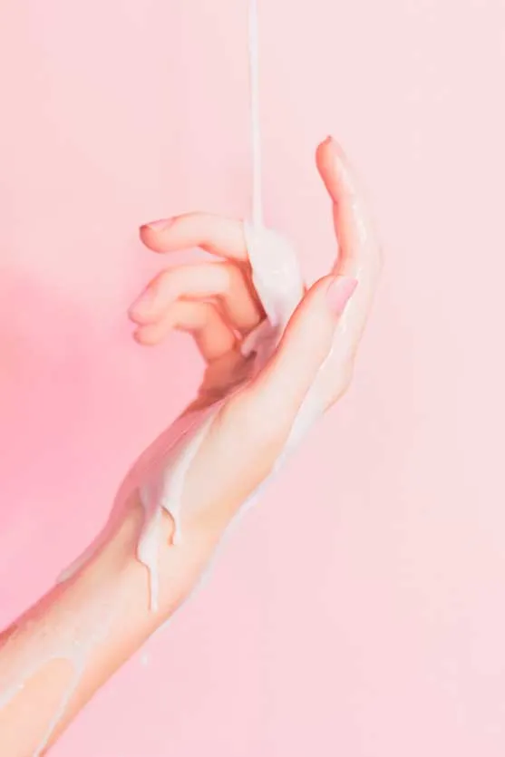 Ilustración de una mano que sostiene un tampón por el hilo, con líquido blanco que escurre, sobre fondo rosa