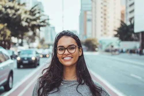 Retrato de una joven sonriente con gafas y cabello largo en una avenida de la ciudad