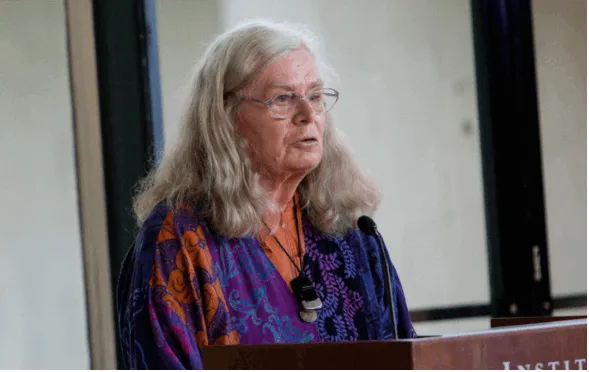 Karen Uhlenbeck, matemática de cabello canoso y gafas, habla con micrófono desde un atril del Instituto de Estudios Avanzados