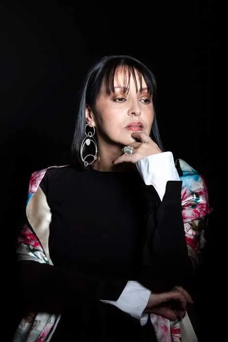 Lucía Ortiz, joyera, posa pensativa con la mano en la barbilla y grandes aretes sobre fondo negro