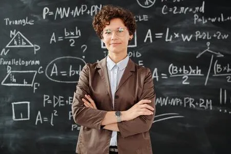 Maestra de pie con los brazos cruzados frente a una pizarra con fórmulas de geometría
