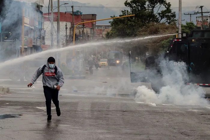 Manifestante corre bajo el chorro de un hidrante y una nube de gas lacrimógeno en una calle