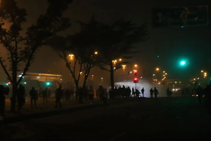 Grupo de manifestantes en una avenida de noche, entre humo y luces de semáforos