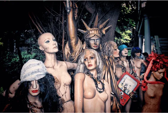 Maniquíes de mujer desnudos con pañuelos, cadenas y una réplica de la Estatua de la Libertad entre árboles