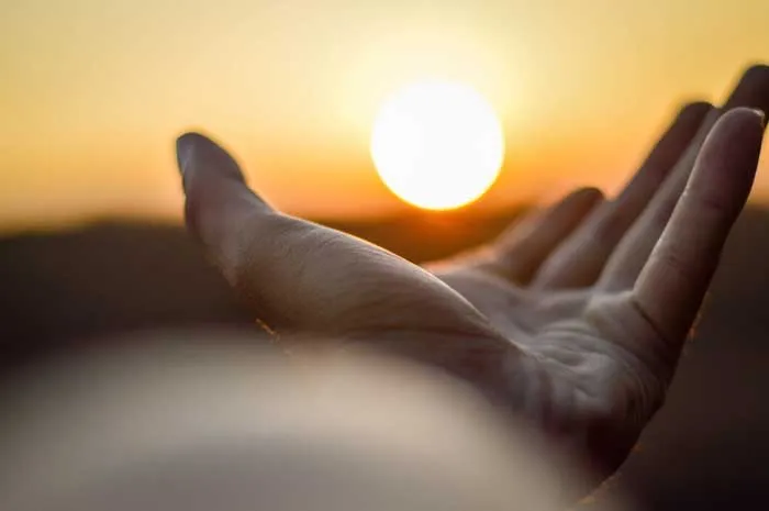 Mano abierta en primer plano frente al sol durante un atardecer