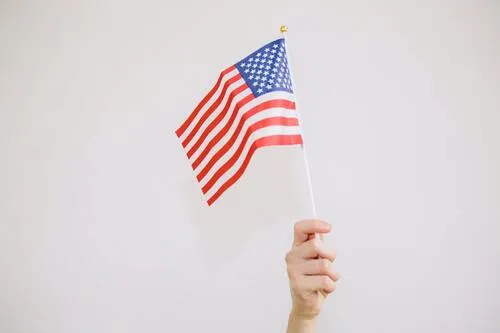 Mano sosteniendo una pequeña bandera de Estados Unidos sobre fondo claro
