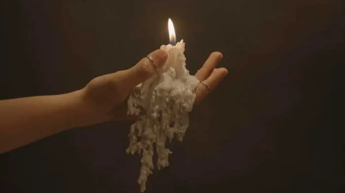 Mano sostiene una vela encendida cubierta de cera derretida en la oscuridad