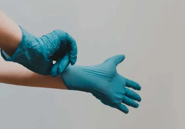 Manos se colocan un guante de látex azul sobre fondo gris