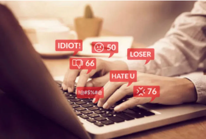 Manos escribiendo en un portátil con burbujas de comentarios de odio como «Idiot!», «Loser» y «Hate u»