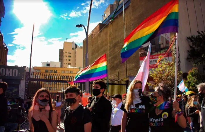 Asistentes con mascarilla y banderas arcoíris en alto frente a un edificio durante la Marcha del Orgullo