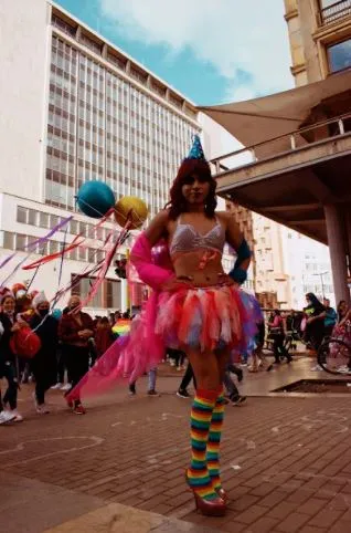 Persona con tutú rosa, medias de rayas de colores y sombrero de fiesta camina por la calle en la Marcha del Orgullo