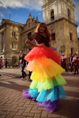 Persona con un vestido de tul de colores del arcoíris posa frente a una iglesia histórica en Bogotá