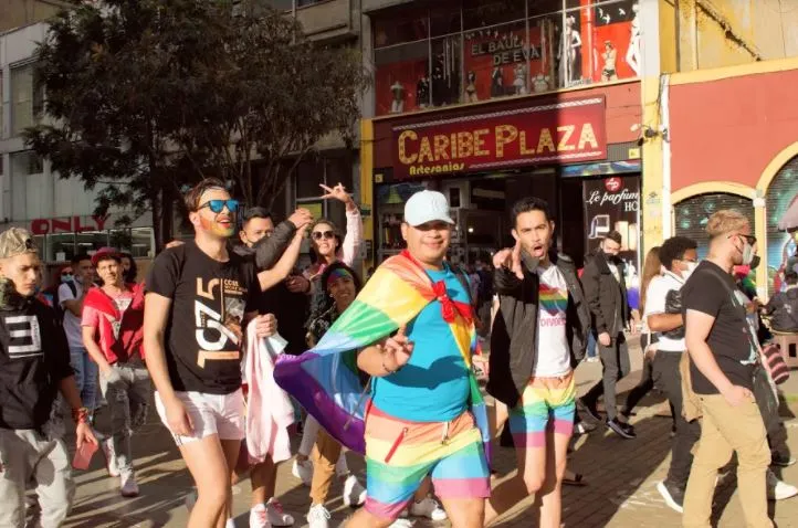 Personas caminan por la calle, una con una bandera arcoíris sobre los hombros, durante la Marcha del Orgullo