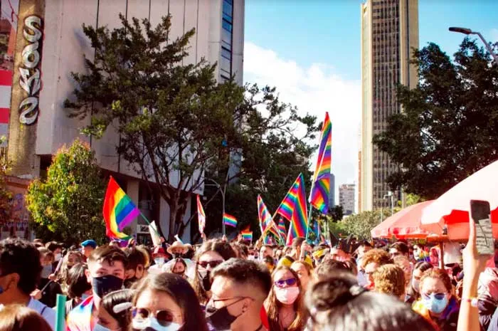Multitud con banderas arcoíris llena una avenida flanqueada por edificios durante la Marcha del Orgullo