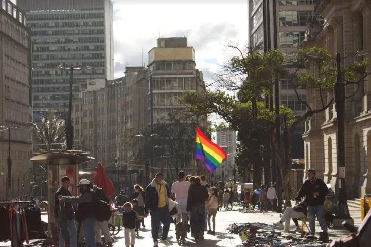 Plaza de Bogotá con transeúntes, edificios altos y una bandera arcoíris ondeando