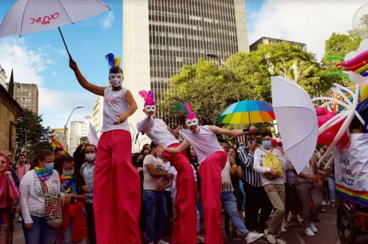 Zancudos con máscaras, trajes rojos y sombrillas blancas avanzan entre la multitud de la Marcha del Orgullo