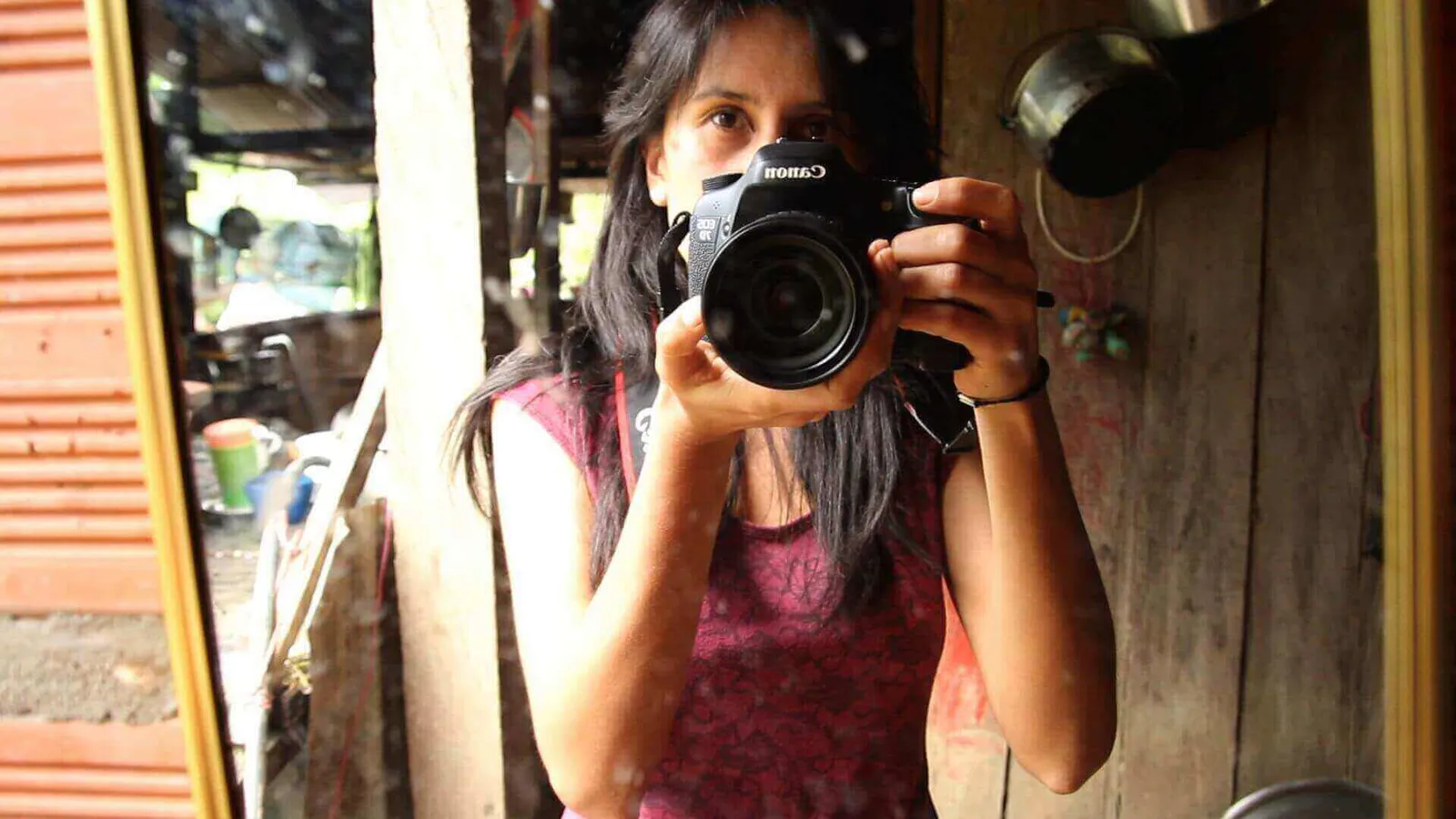 Mujer se fotografía frente a un espejo con una cámara réflex en una casa de madera