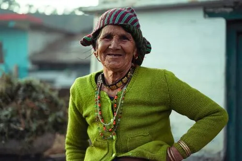 Mujer mayor sonriente con gorro tejido, cárdigan verde y collares de colores, con la mano en la cintura