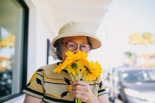 Mujer mayor con sombrero y gafas que huele un ramo de girasoles