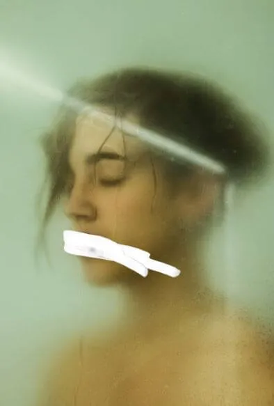 Retrato borroso de una mujer con los ojos cerrados y un trozo de tela blanco atravesado en la boca, en tonos verdes