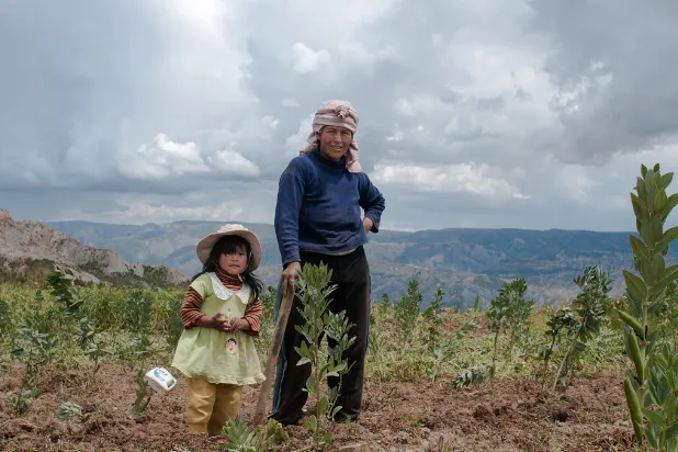 Una mujer y una niña con sombrero en un campo de cultivo con montañas y cielo nublado