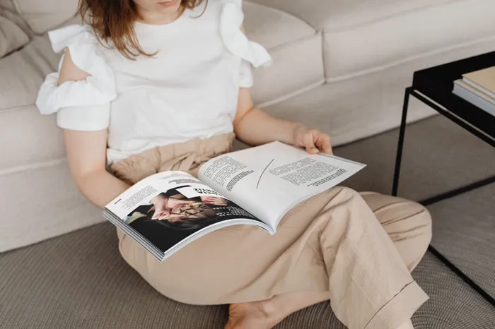 Mujer sentada en un sofá hojea una revista abierta sobre sus piernas
