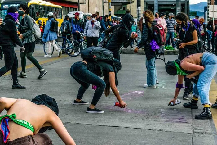 Mujeres agachadas pintan con aerosol el pavimento de una calle concurrida durante la marcha del 8 de marzo