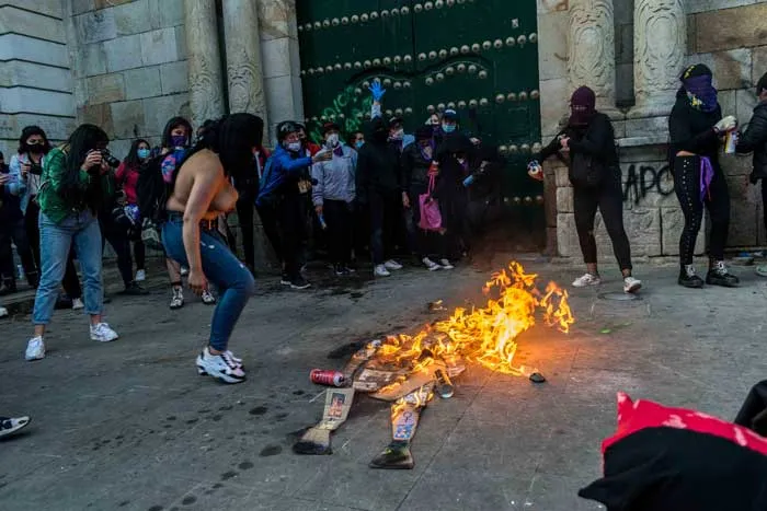 Mujeres encienden una hoguera en la calle frente a un portón verde durante la marcha del 8 de marzo