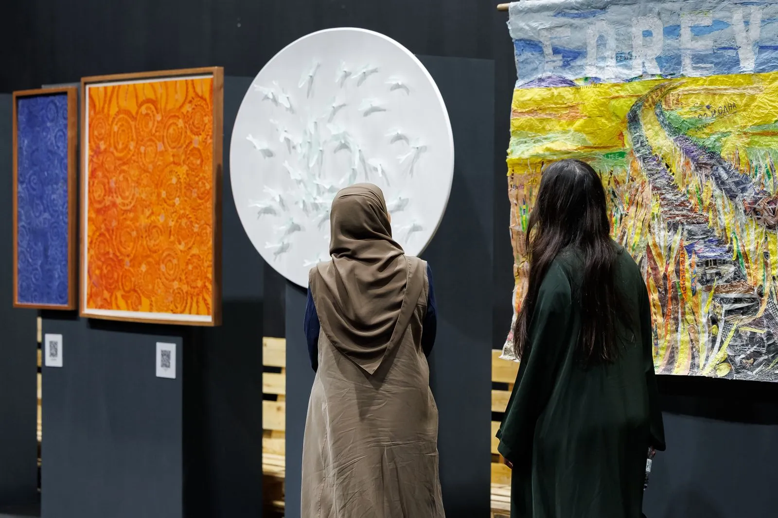 Dos mujeres observan cuadros de colores y una obra circular blanca en una exposición de arte