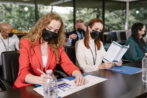Mujeres con tapabocas sentadas en una mesa de conferencia leyendo documentos y folletos